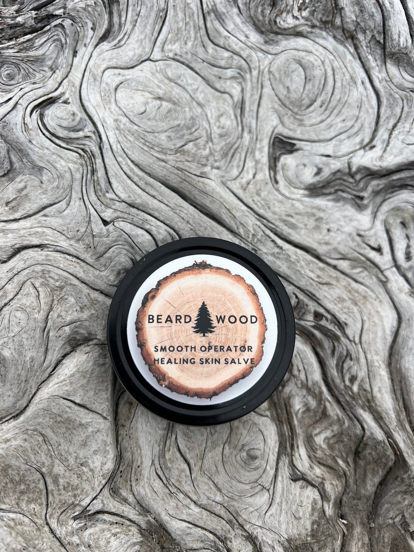 Smooth Operator Healing Skin Salve by Beardwood Beard Oil Co. in Bend, Oregon. The product is in a canister that looks like a tree stump with a black outline. The Beardwood Beard Oil Co. logo is on the front.